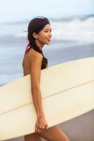 very good looking Asian woman on the beach with a surfboard.